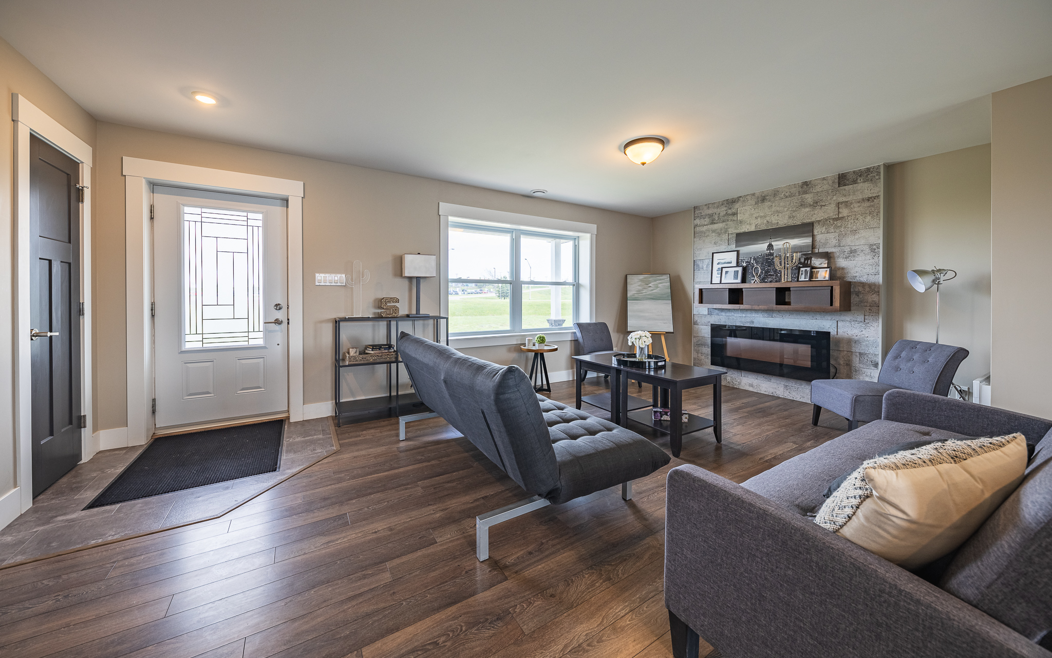 Modern living room with wood flooring, gray sofas, and a black coffee table. A stone feature wall with a fireplace adds warmth, while natural light from a large window creates a cozy atmosphere.