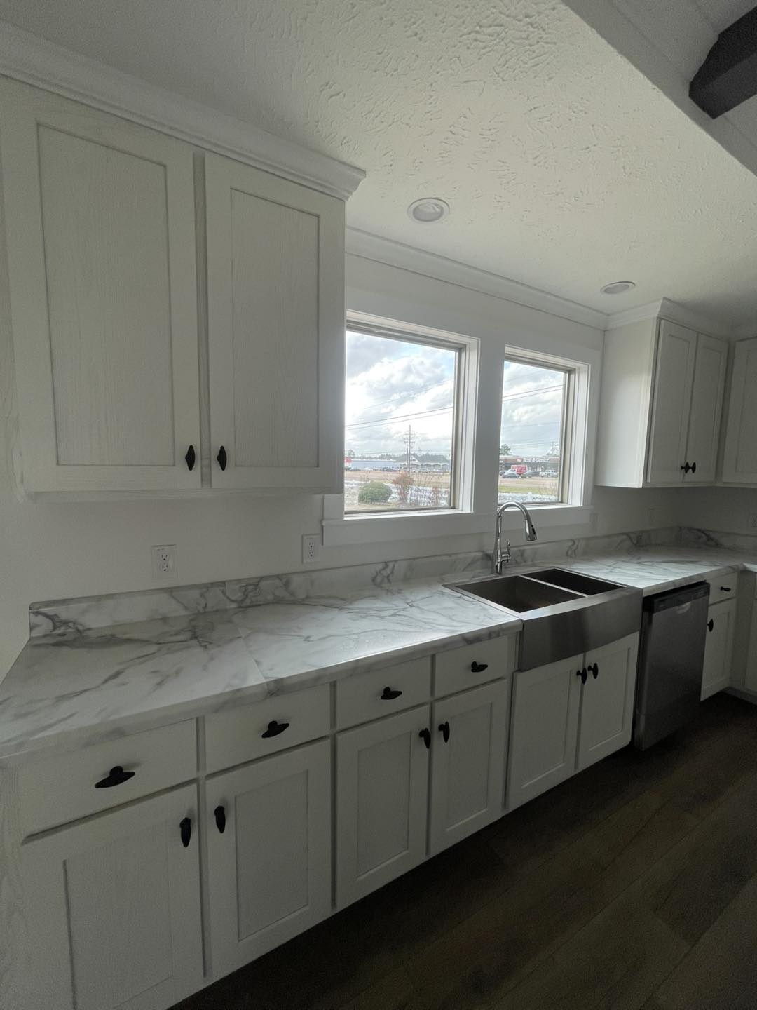Bright kitchen with marble countertops, white cabinets, and stainless steel appliances. Large windows let in natural light, creating a fresh atmosphere.