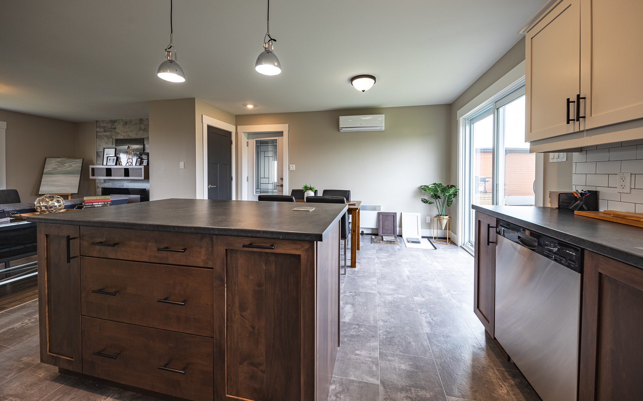 Modern kitchen and dining area with wooden cabinetry and island, stainless steel appliances, and sliding glass doors. The room has a bright, airy feel.