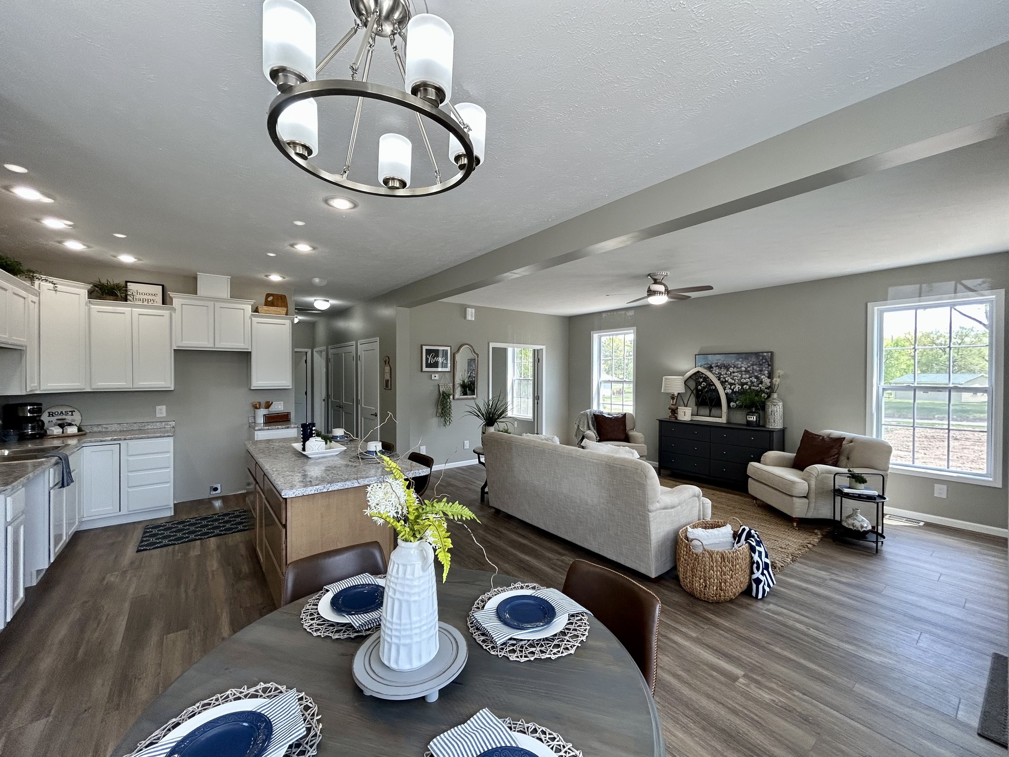 Spacious open-concept living and dining area with modern lighting. Features white kitchen cabinets, an island, cozy seating, and large windows.