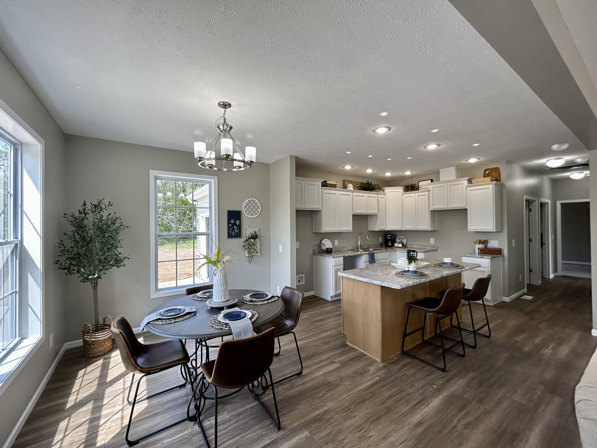 Bright, modern kitchen-dining area with wood floors. A round table set for four is near large windows, alongside an island with bar stools. Cozy and inviting.