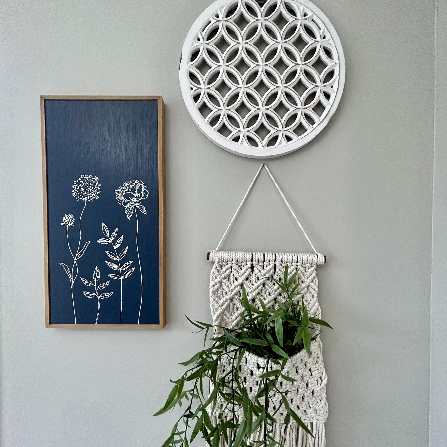 Wall decor with a white circular pattern, a navy floral print, and a macramé hanger holding greenery. The tone is bohemian and serene.