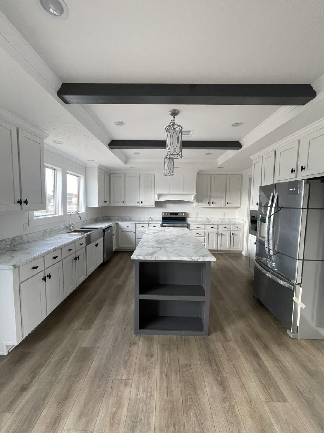 Spacious kitchen with white cabinets, marble countertops, a central island, stainless steel appliances, wooden floors, and pendant lighting.
