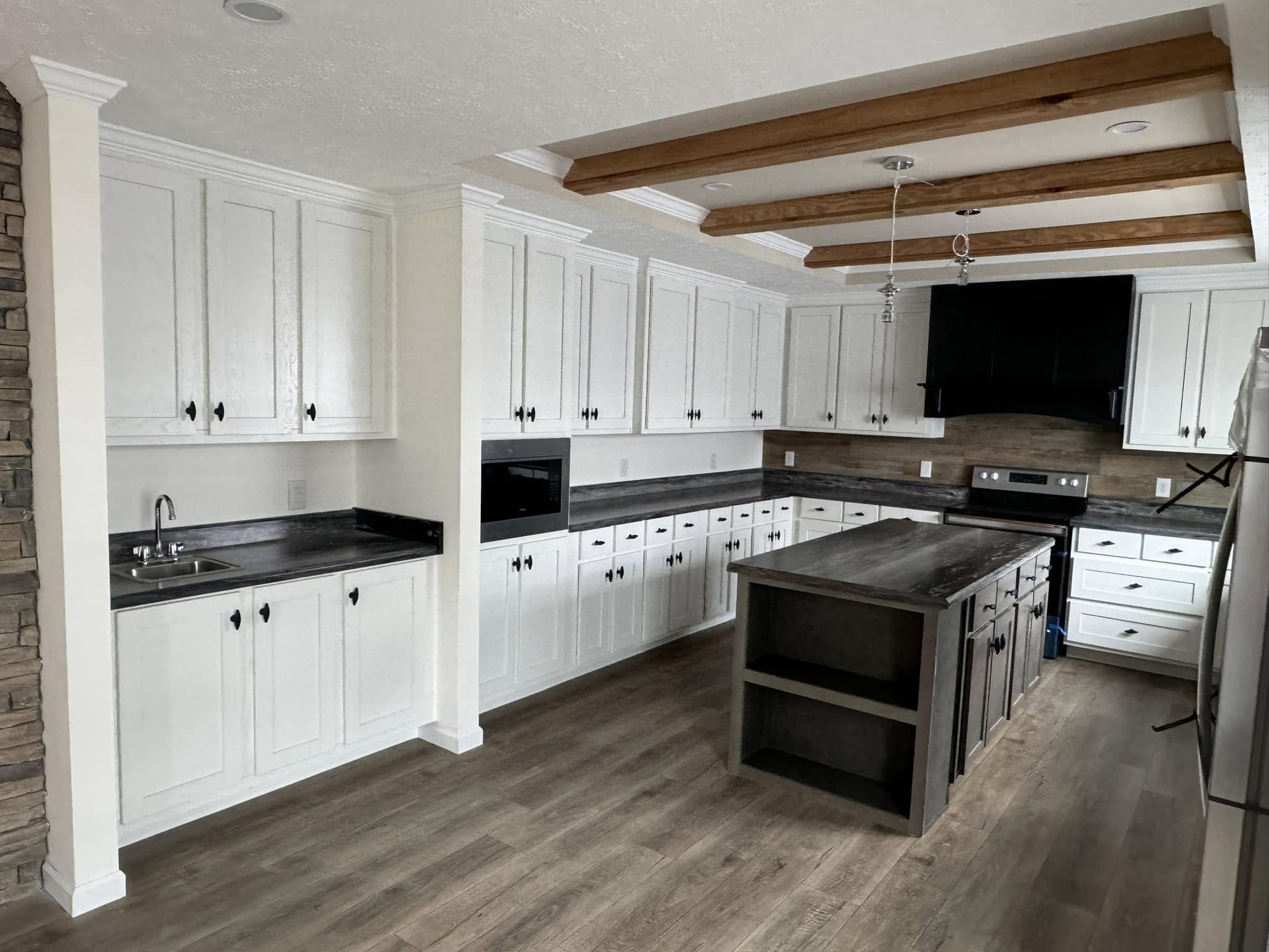 Modern kitchen with white cabinets, dark countertops, and a central island with wooden beams overhead. Hardwood floors add warmth and elegance.
