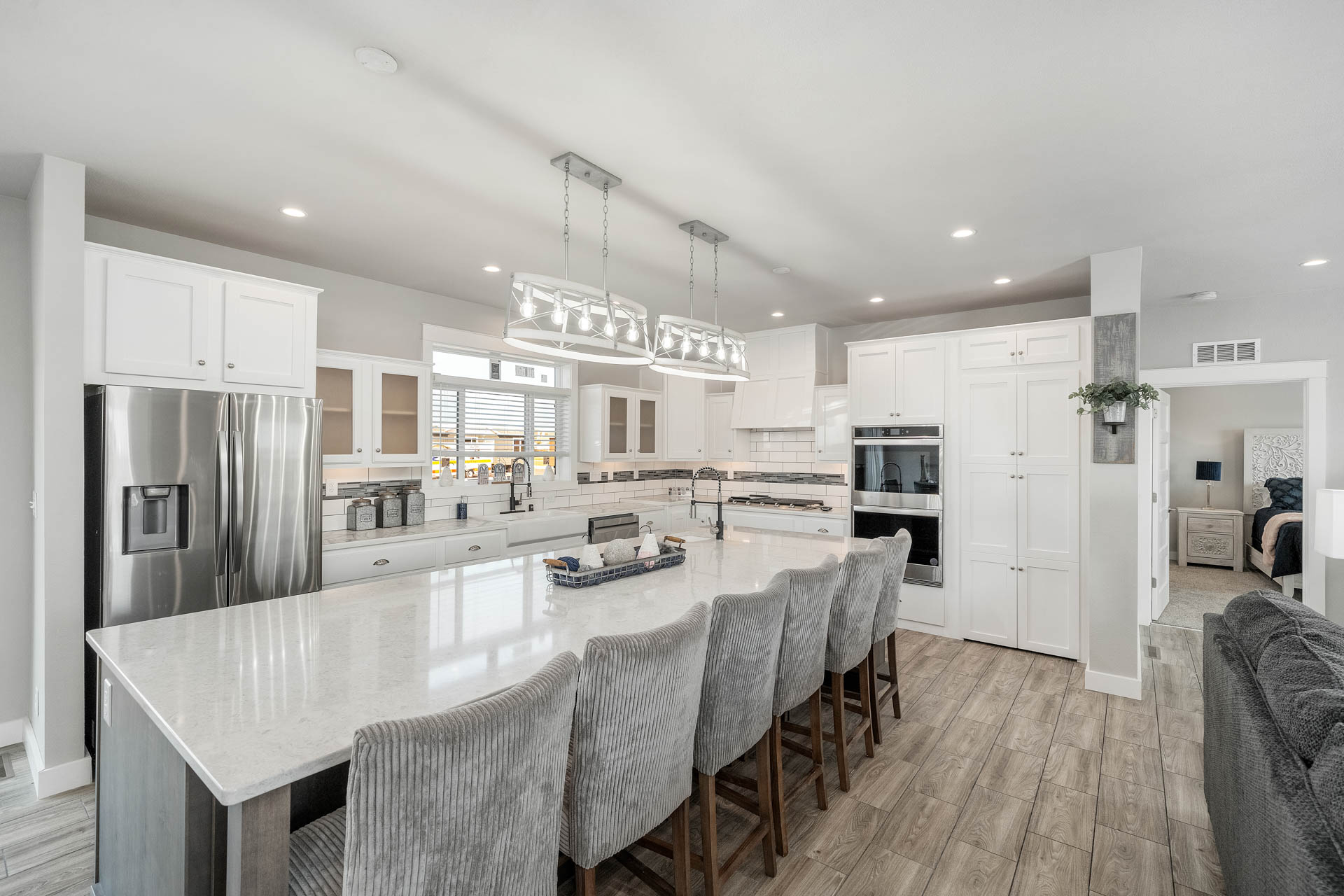 Spacious modern kitchen, featuring a large white island with gray upholstered chairs, stainless steel appliances, and sleek white cabinets; bright and welcoming.