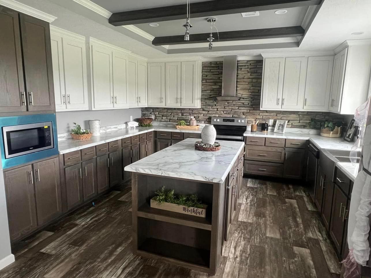 Modern kitchen with two-tone cabinets; white upper and dark lower, stone backsplash, marble island, and dark wood floor. Warm and stylish atmosphere.