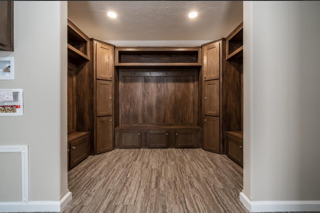 A cozy entryway features dark wood built-in cabinets, a bench, and hooks under warm lighting. The space is inviting and well-organized.