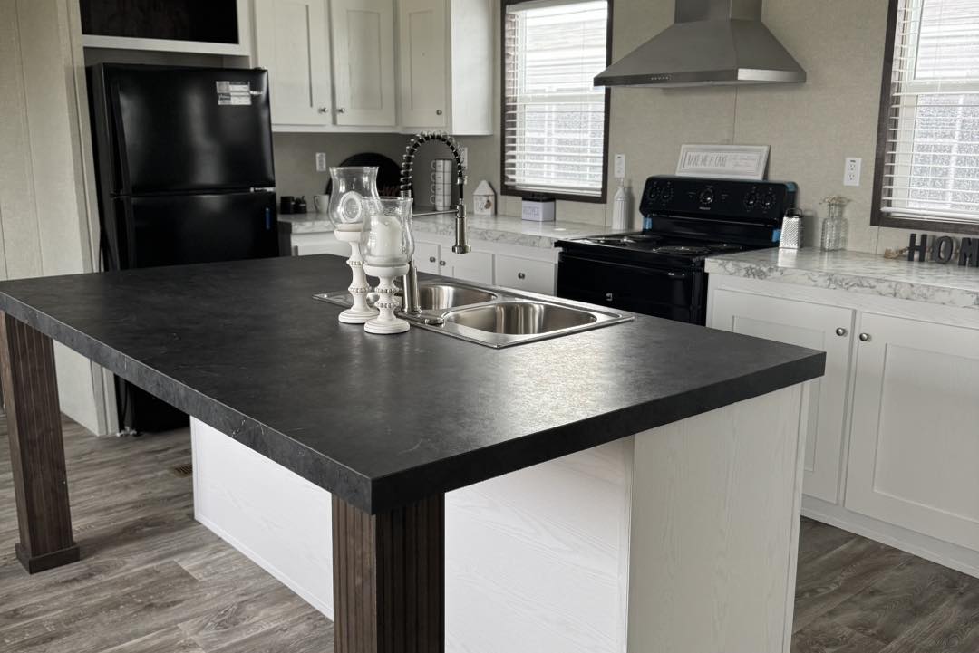 Modern kitchen with white cabinetry, a black countertop island featuring a sink and decor, stainless steel stove, black fridge, and wooden flooring.