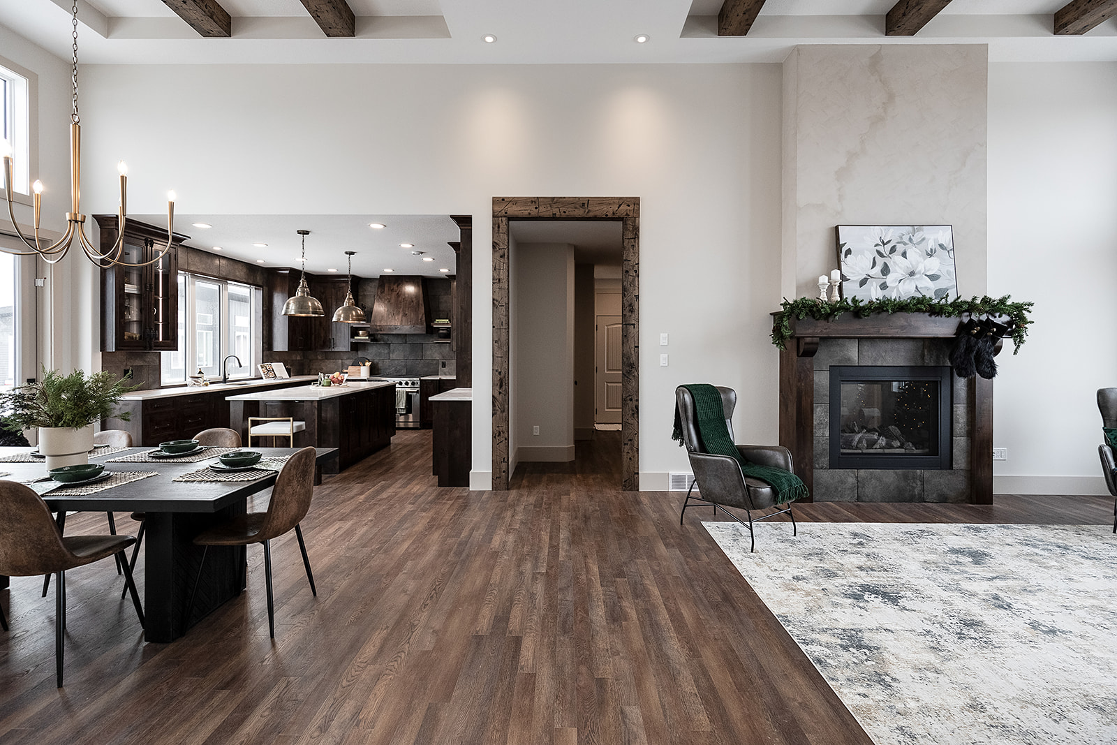 Spacious modern living area with dark wood kitchen, elegant dining set, and cozy fireplace. Features high ceilings, exposed beams, and warm tones.
