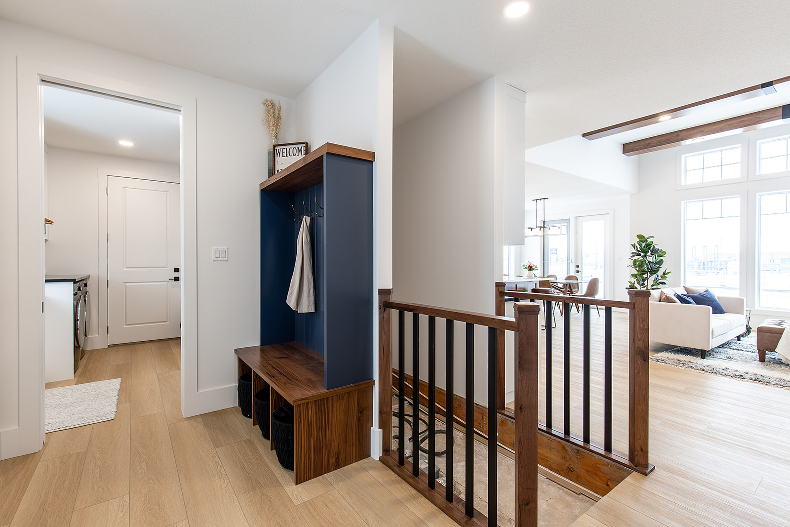Modern home interior with a cozy entryway featuring a wooden bench and hooks, adjacent to a bright, open living area with large windows and light wood flooring.