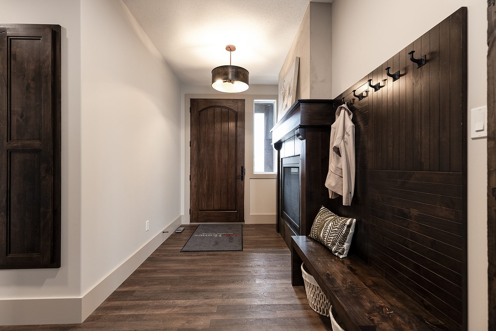 Spacious hallway with dark wood accents, including a door, bench, and coat hooks. A warm glow from a ceiling light creates an inviting atmosphere.