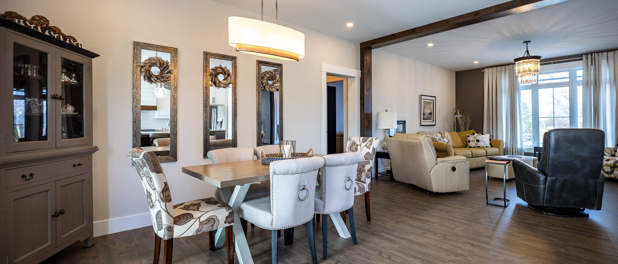 Modern open-concept living and dining area with elegant decor. Features a wooden dining table, cushioned chairs, mirrors, and a cozy seating area with large windows.
