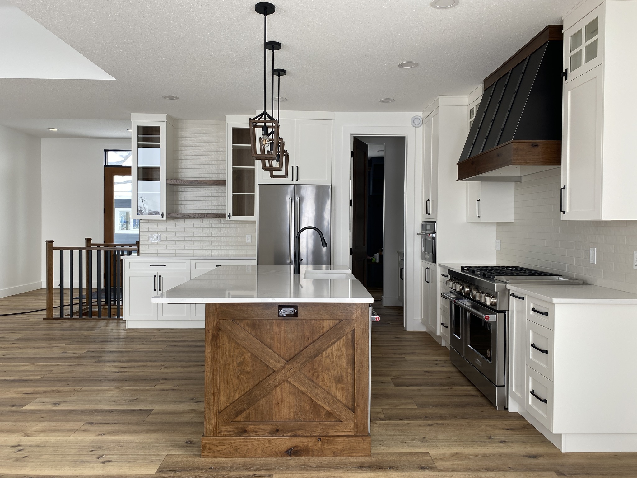 Spacious modern kitchen with white cabinets, wooden island, stainless steel appliances, and pendant lights. Hardwood floors add warmth.