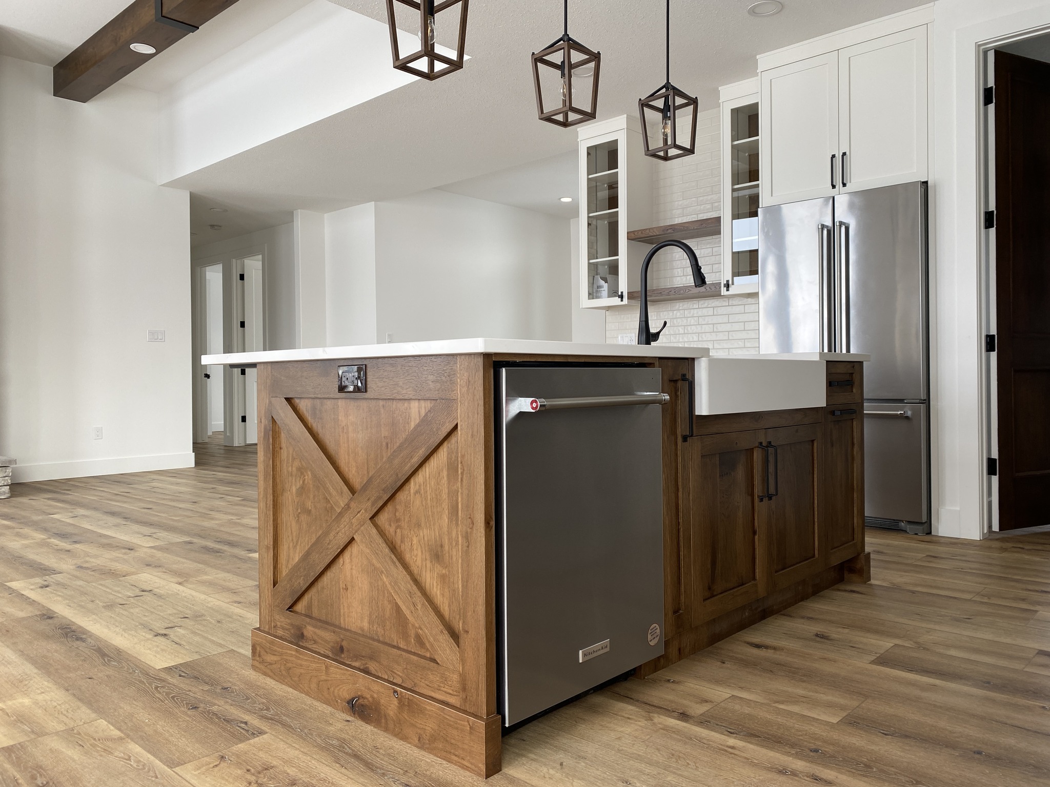 Modern kitchen with a wooden island and gray dishwasher, pendant lights above. Features light wood flooring, white cabinets, and stainless steel fridge.