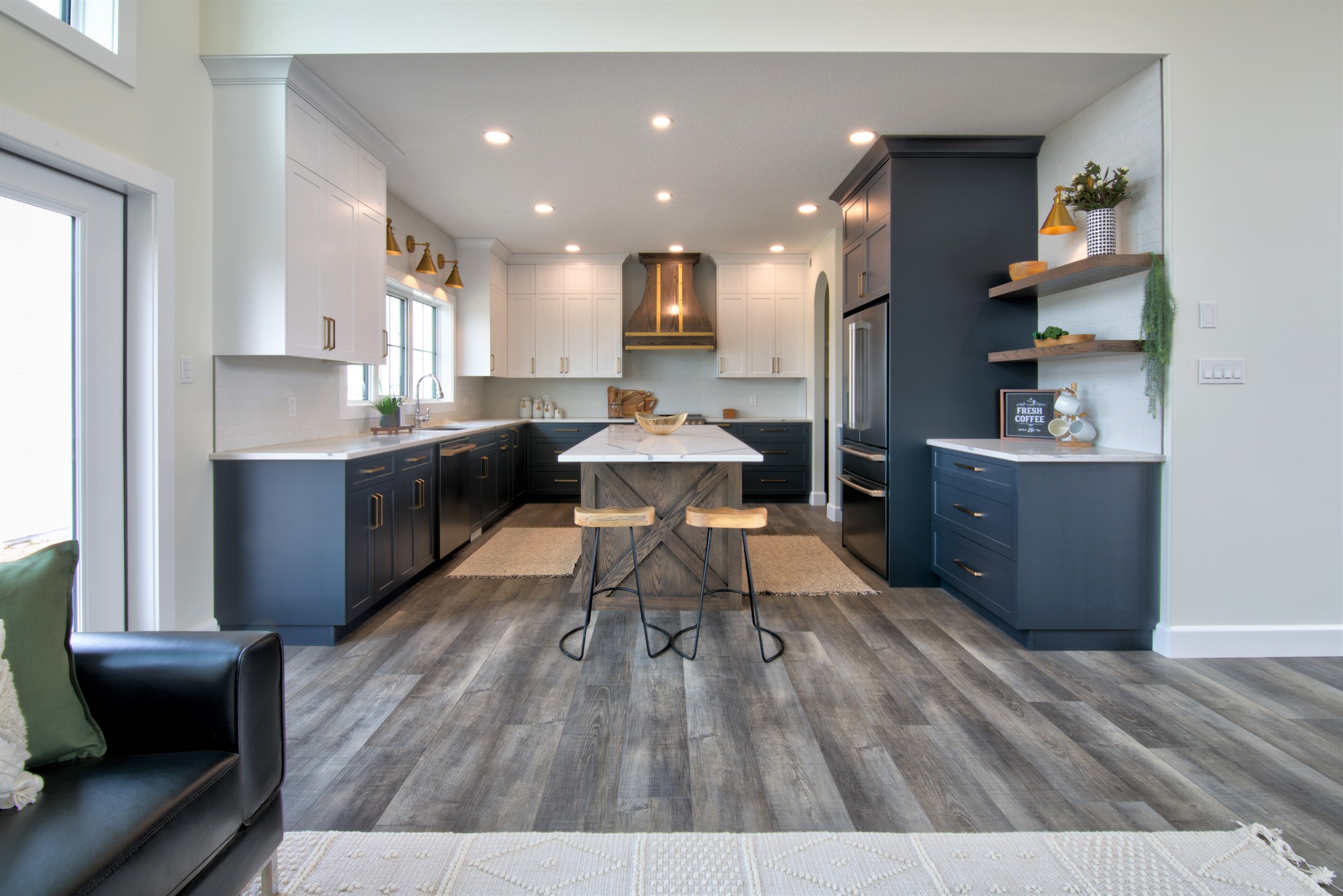 Modern kitchen with sleek white and dark blue cabinets, a center island with two wooden stools, and wooden flooring. Bright and spacious ambiance.