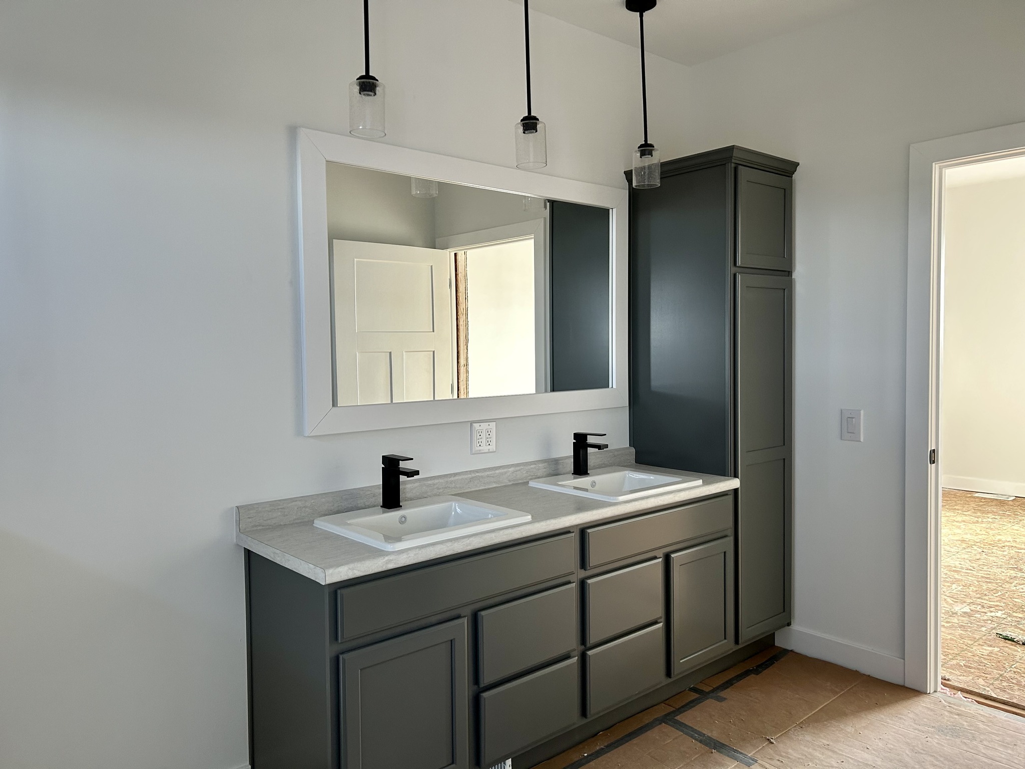 Modern bathroom with a large mirror above a dual sink vanity. Dark cabinets, black faucets, and hanging pendant lights create a sleek, minimalistic look.