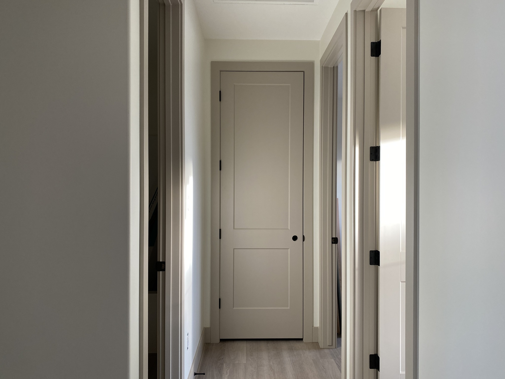A narrow hallway with soft, natural light features three closed beige doors on the left, right, and end. The clean, minimalist setting conveys calm.
