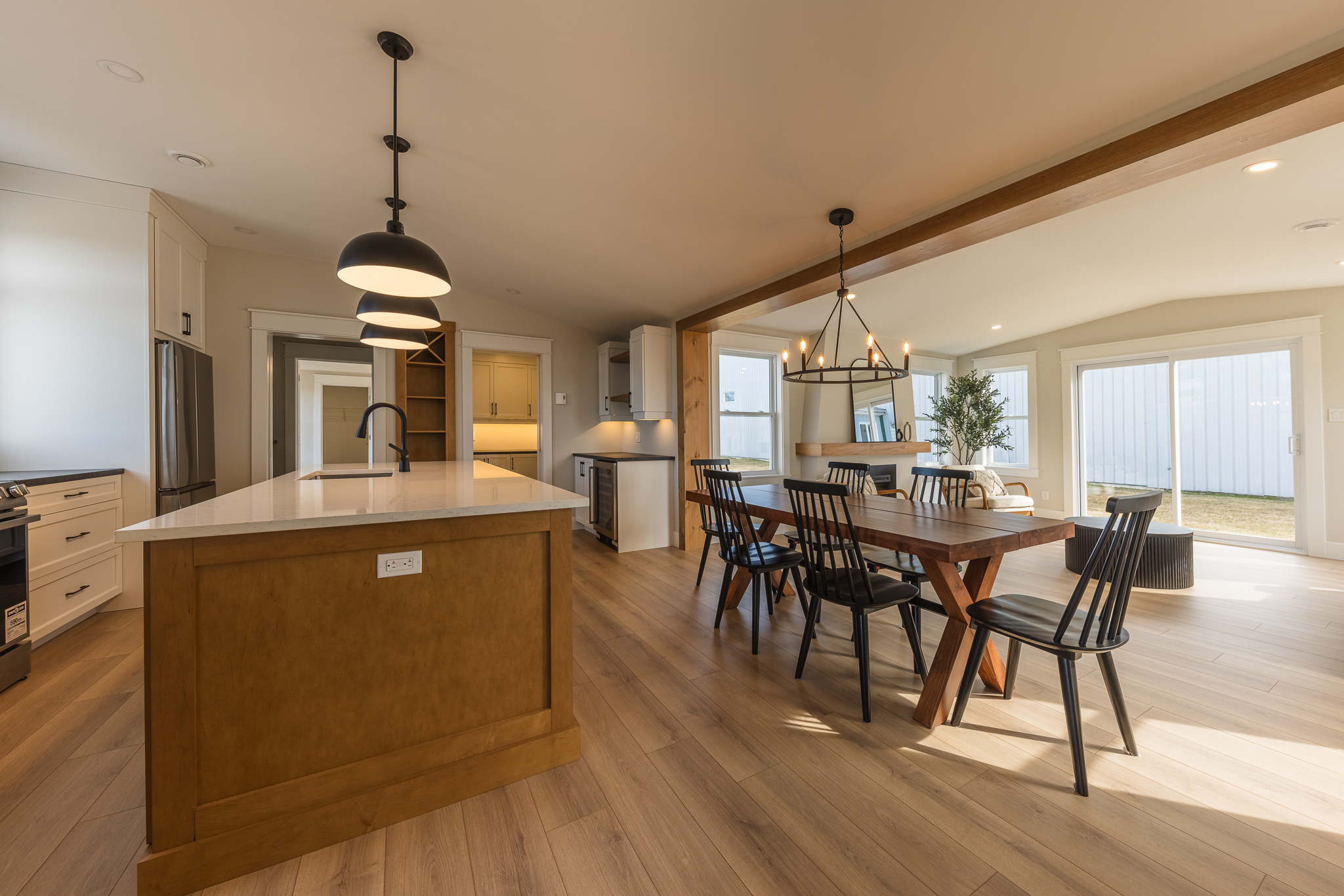 Spacious modern kitchen and dining area with wooden floors. Features island with pendant lights, long wooden table, black chairs, large windows.
