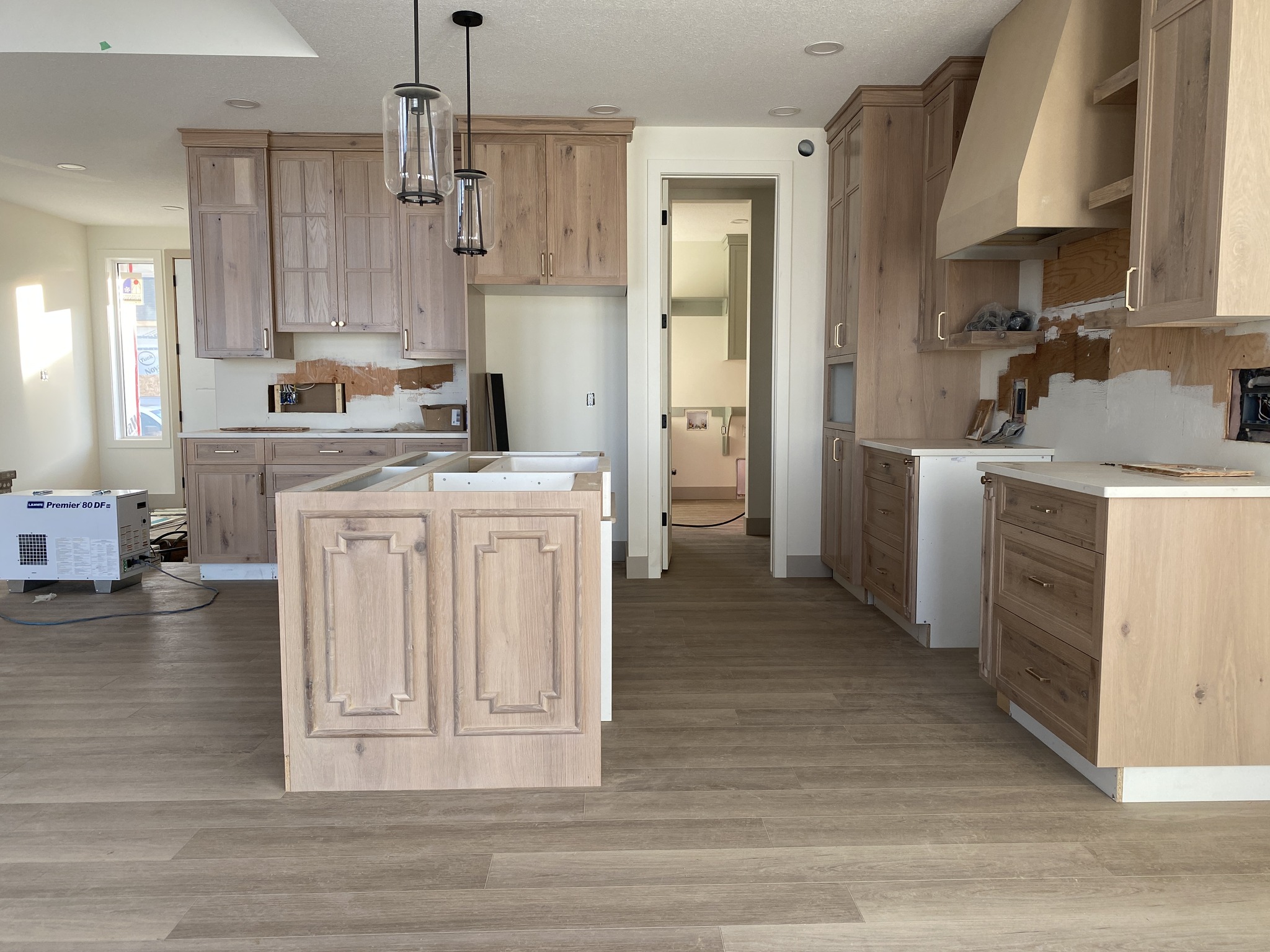 Spacious kitchen under renovation with light wood cabinets, unfinished countertops, and a central island. Pendant lights hang from the ceiling.