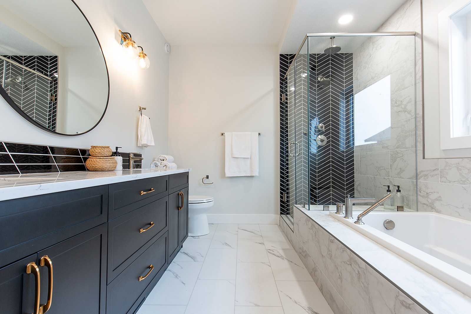 Modern bathroom with a sleek design features a large mirror above a dark vanity, gold accents, glass shower, and marble tiles, creating a calm ambiance.