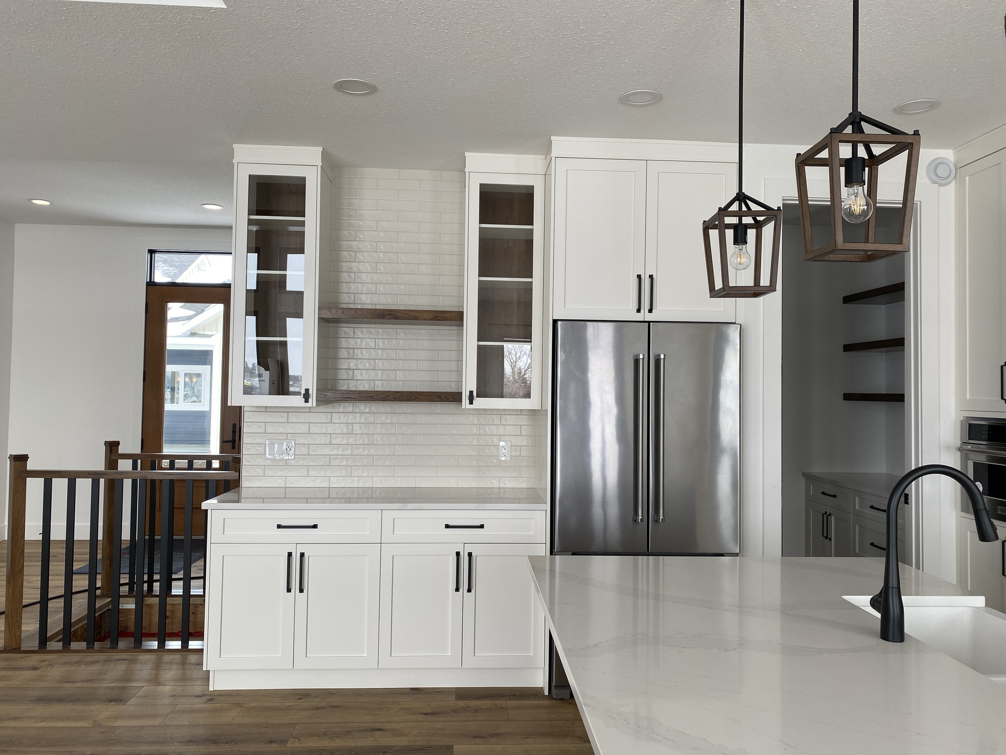 Modern kitchen with white cabinets, brick backsplash, stainless steel fridge, and wood accents. Features a sleek black faucet and pendant lights.