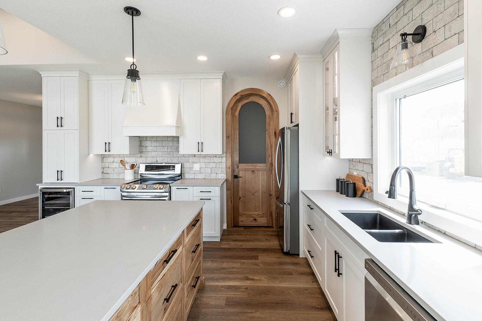 Modern kitchen with white cabinets, wood island, and stainless steel appliances. Brick accent wall, arched wooden door, large window, and a sleek faucet create a warm, inviting atmosphere.