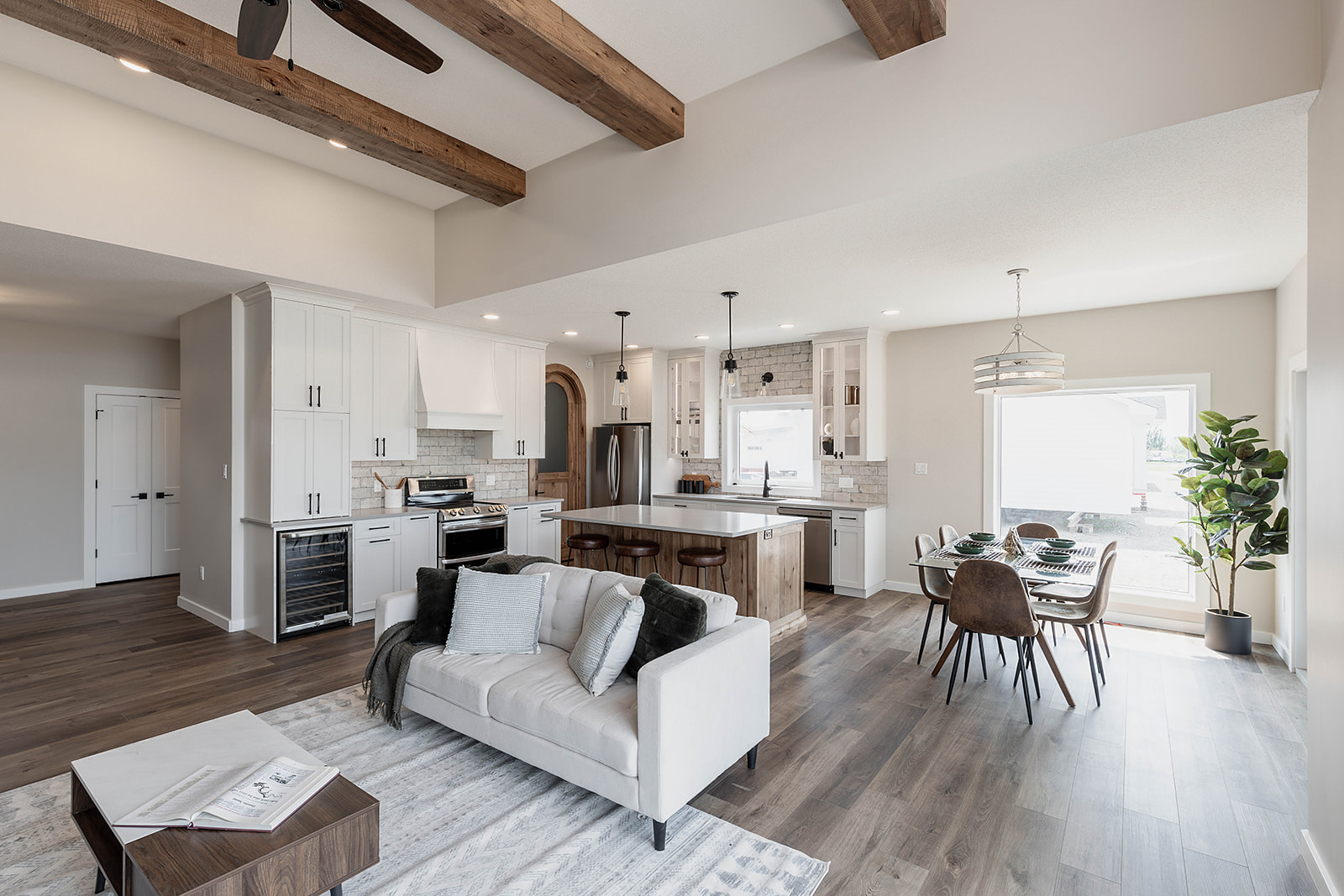 Modern open-concept living space featuring a cozy sofa, wooden beams, a sleek kitchen with white cabinets, and a dining area with abundant natural light.