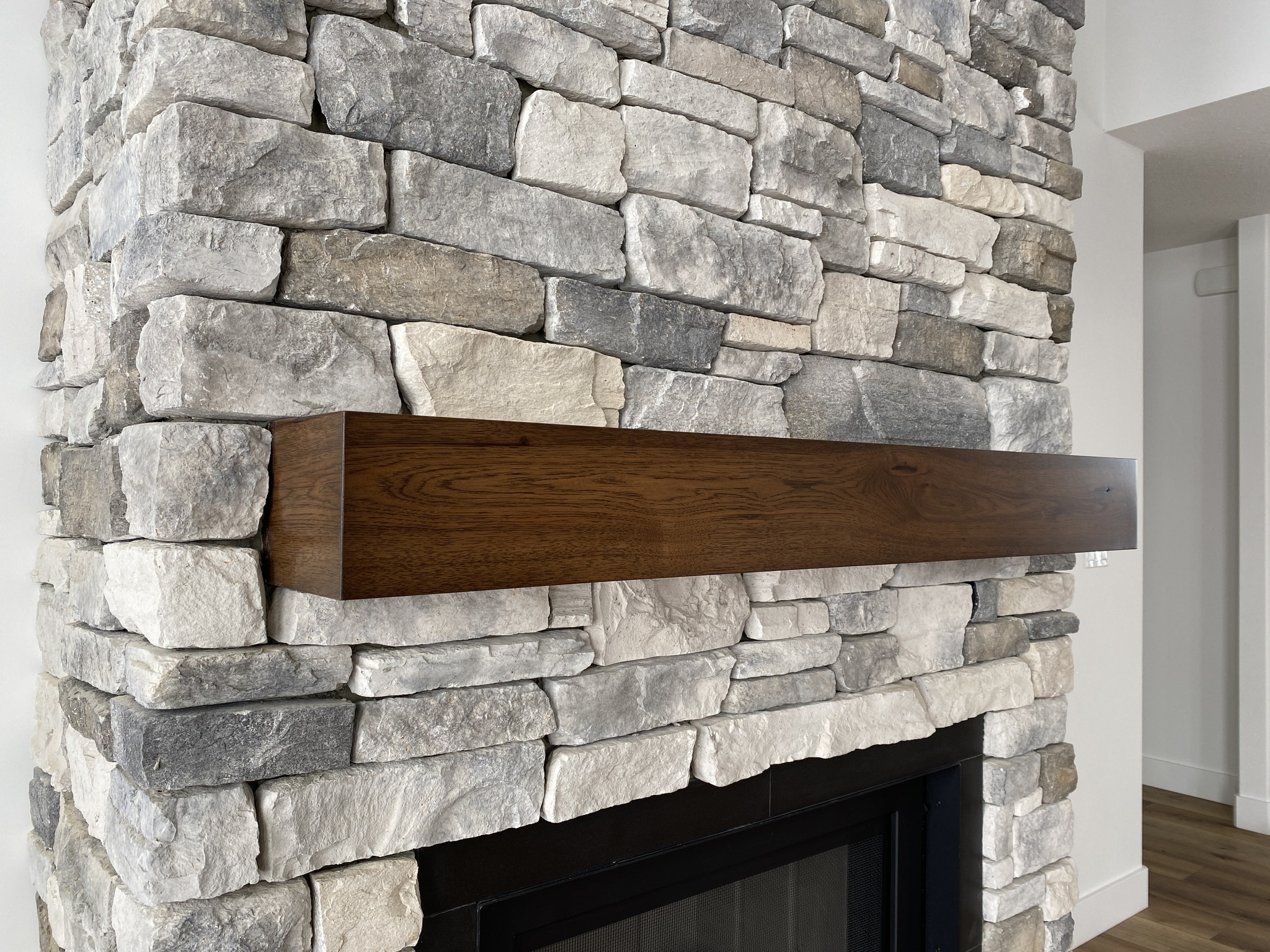 Stone fireplace with a smooth, dark wooden mantel. The rough, multicolored stonework contrasts with the polished wood, creating a rustic yet modern feel.