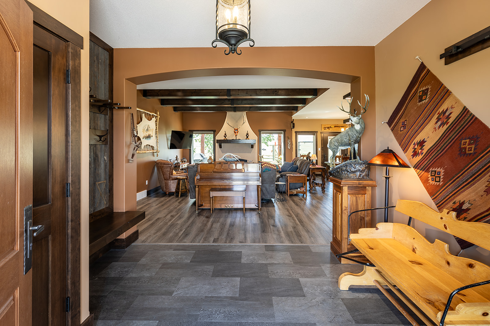 Modern bathroom with warm beige walls, dual sinks with marble countertops, a soaking tub, glass shower, wooden shelves, and rustic decor elements.