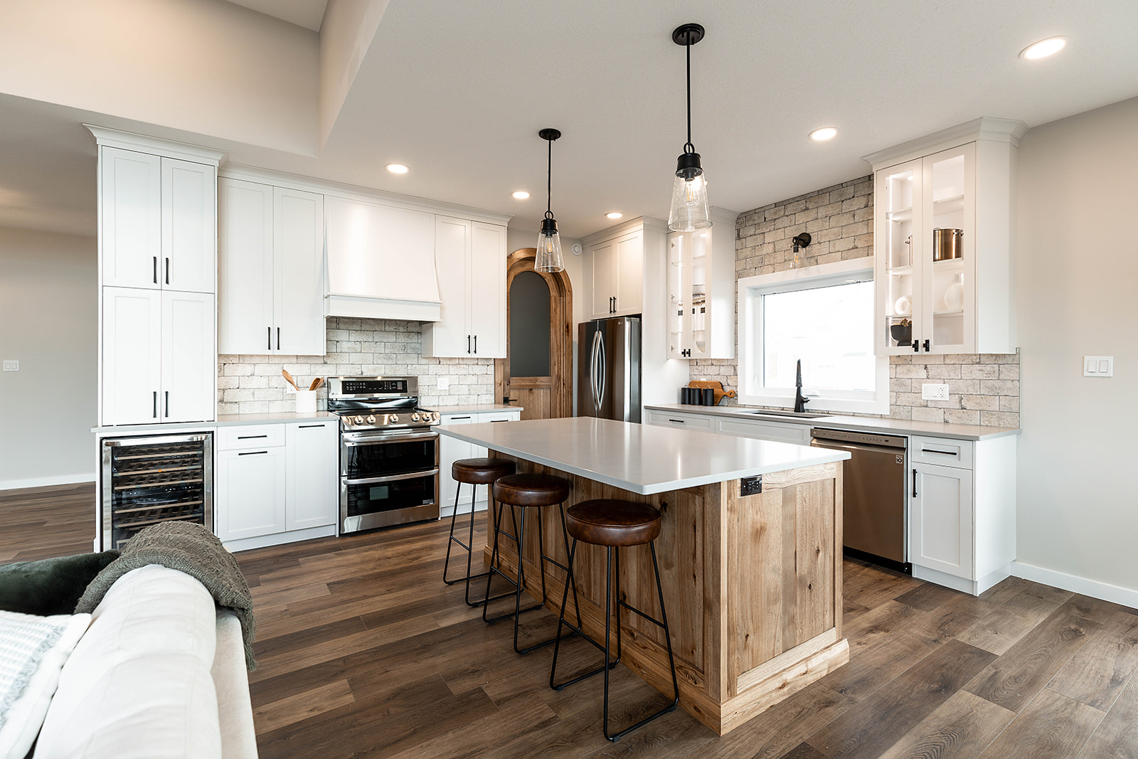 Modern kitchen with white cabinetry, stainless steel appliances, and a large wooden island with stools. Warm lighting and subway tile accent wall.