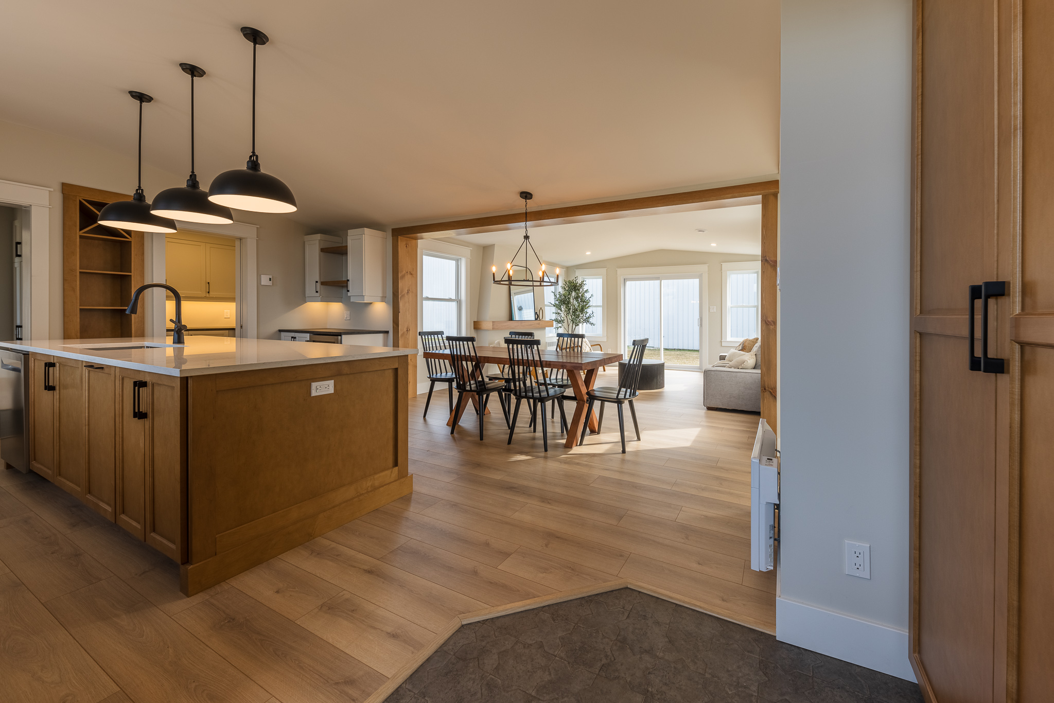 Spacious kitchen and dining area with wooden floors and modern lighting. An island with pendant lights, dining table, large windows, and bright, airy vibe.