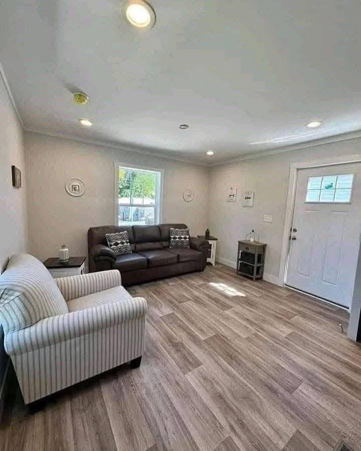 Cozy living room with a striped armchair and a brown leather sofa, wooden floor, soft lighting, and a small table near the door. Calm and inviting atmosphere.