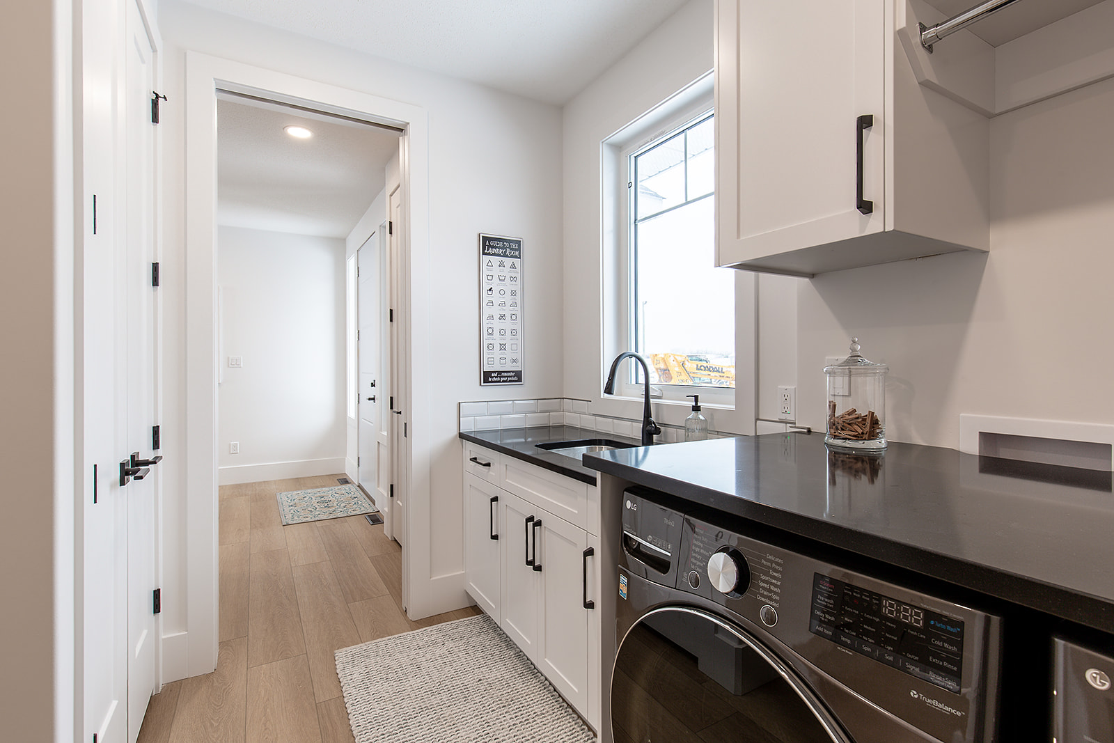 Modern laundry room with white cabinets, a black countertop, and a washing machine. Bright light from a window illuminates the tidy space.