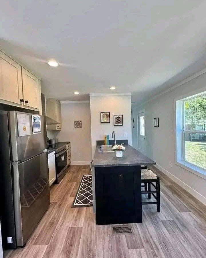 Modern kitchen with wooden floors, stainless steel appliances, and a dark countertop island. Large window provides natural light. Cozy and inviting.