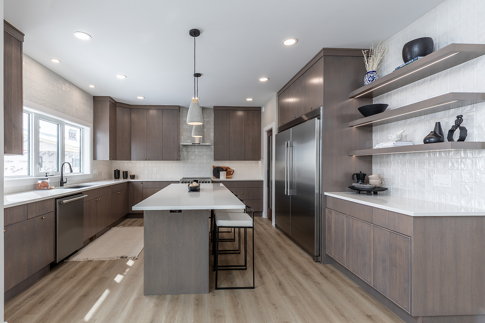 Modern kitchen with a sleek design featuring dark wood cabinets, a central island with white countertop and bar stools, and stainless steel appliances.