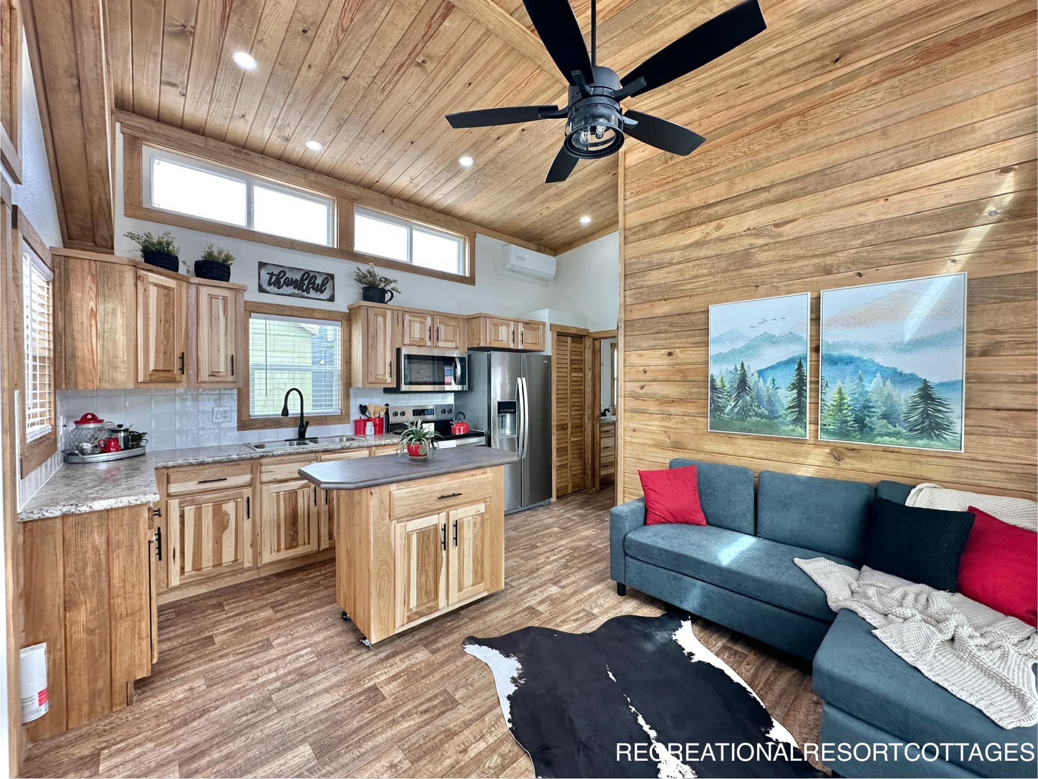 Rustic kitchen and living area with wood accents, granite countertops, stainless steel appliances, and cozy sofa. Bright, airy, and welcoming atmosphere.
