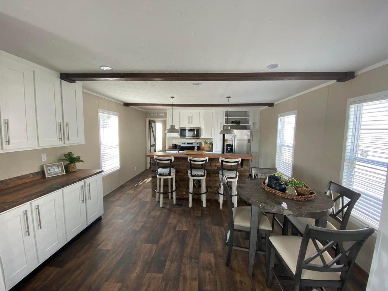 Spacious modern kitchen with white cabinets, a wood island, and pendant lights over bar stools. Cozy dining area with a round table and a fruit basket.
