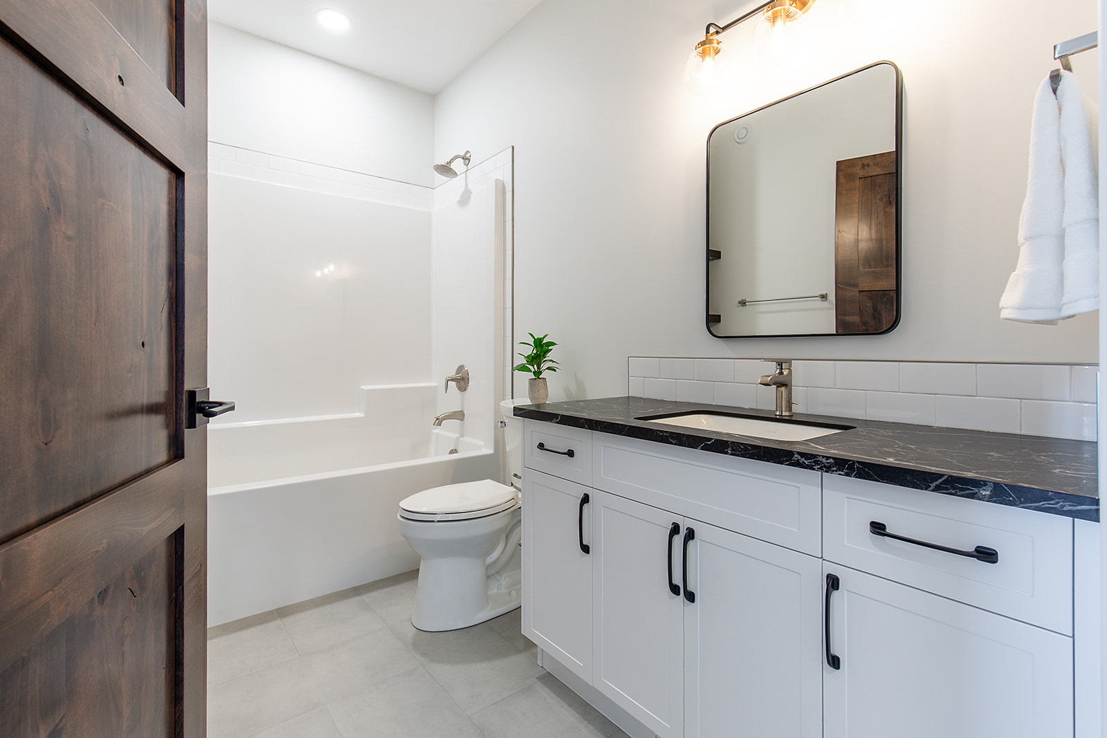 Modern bathroom with a white vanity, black countertop, and a rectangular mirror. Features a bathtub, toilet, and soft overhead lighting, creating a clean, serene feel.