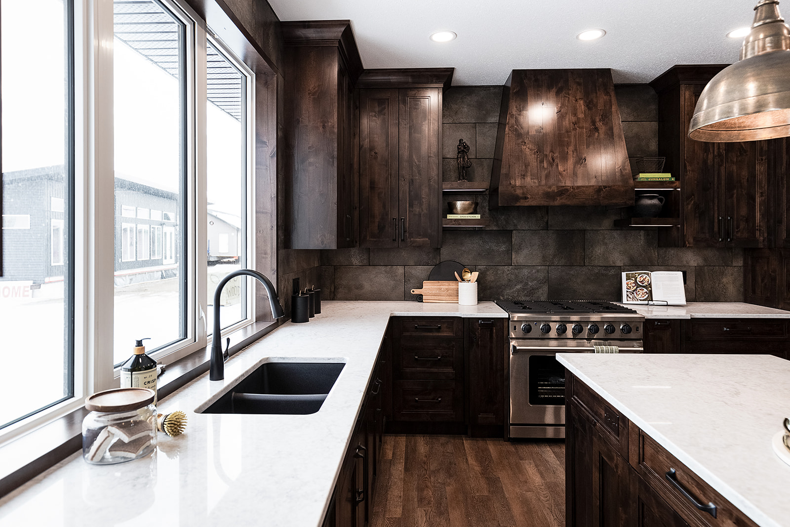 Sleek kitchen with dark wood cabinets, marble countertops, and a stainless steel stove. Bright natural light from large windows creates a warm, modern feel.