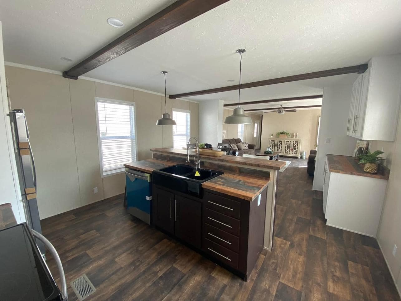 Spacious, modern kitchen with dark wood floors, exposed beams, and pendant lights. Black sink and appliances contrast white cabinets and walls. Calm and inviting atmosphere.