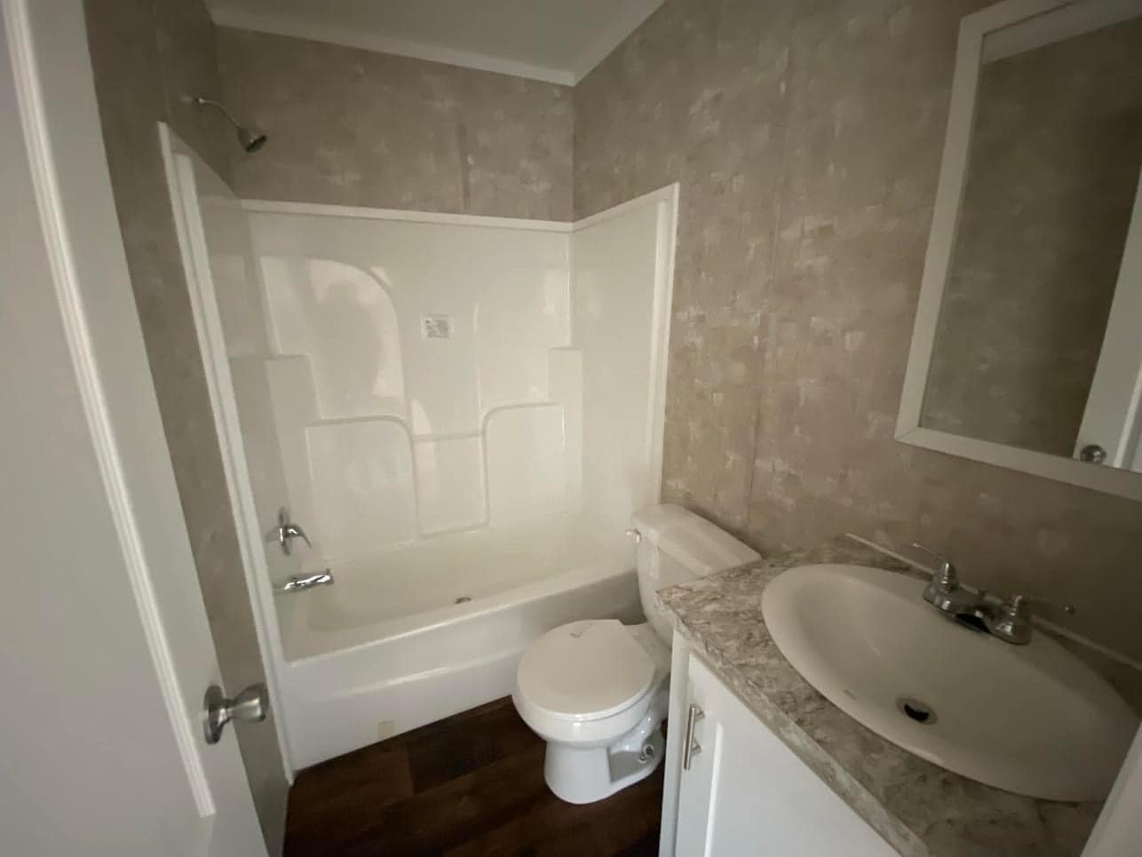 Small bathroom with white bathtub-shower combo, beige marble counter with sink, toilet, and muted patterned wallpaper. Warm, functional vibe.