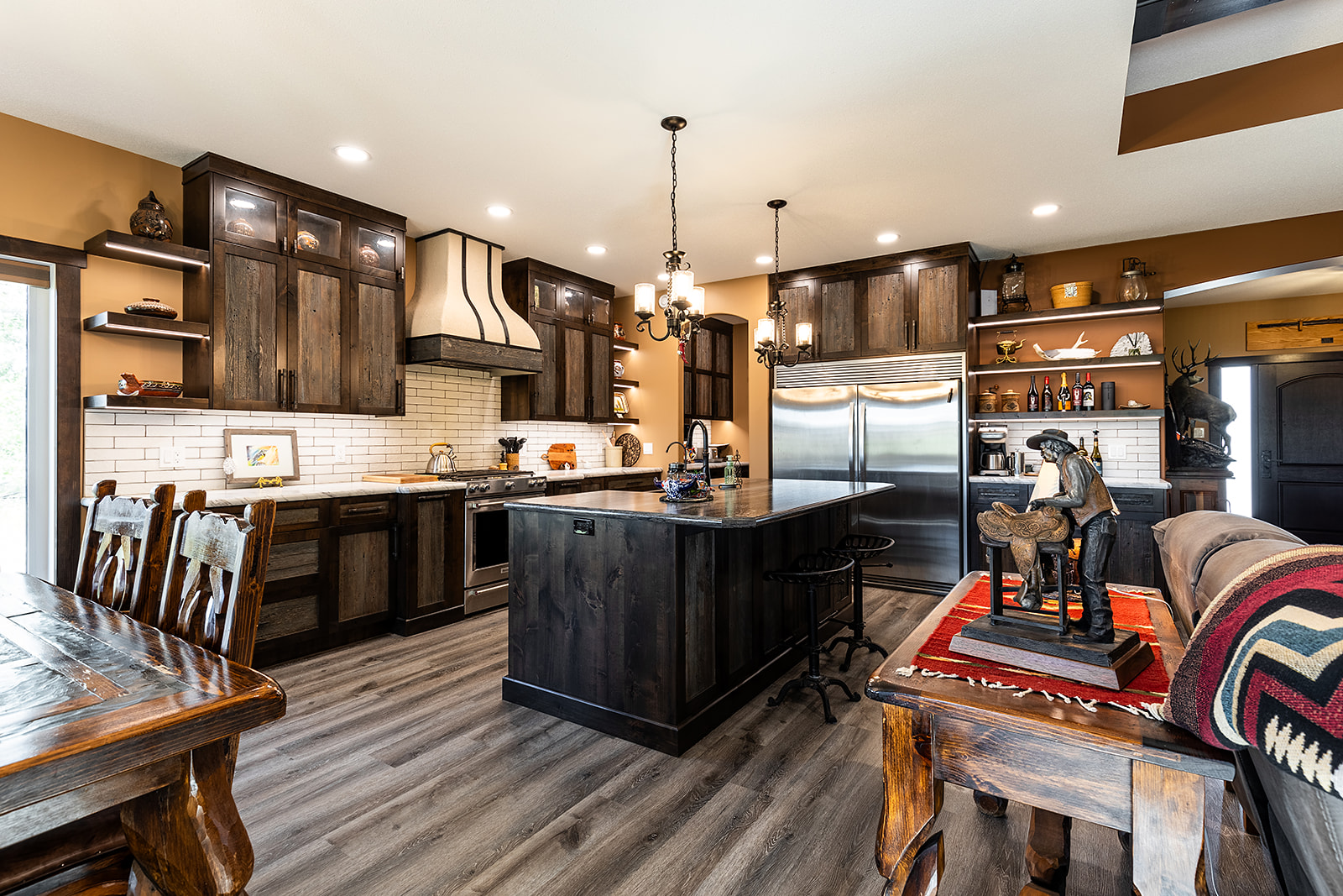 Rustic kitchen with dark wood cabinets, central island, and stainless steel appliances. A cozy dining area has a wooden table and tribal decor. Warm, inviting atmosphere.