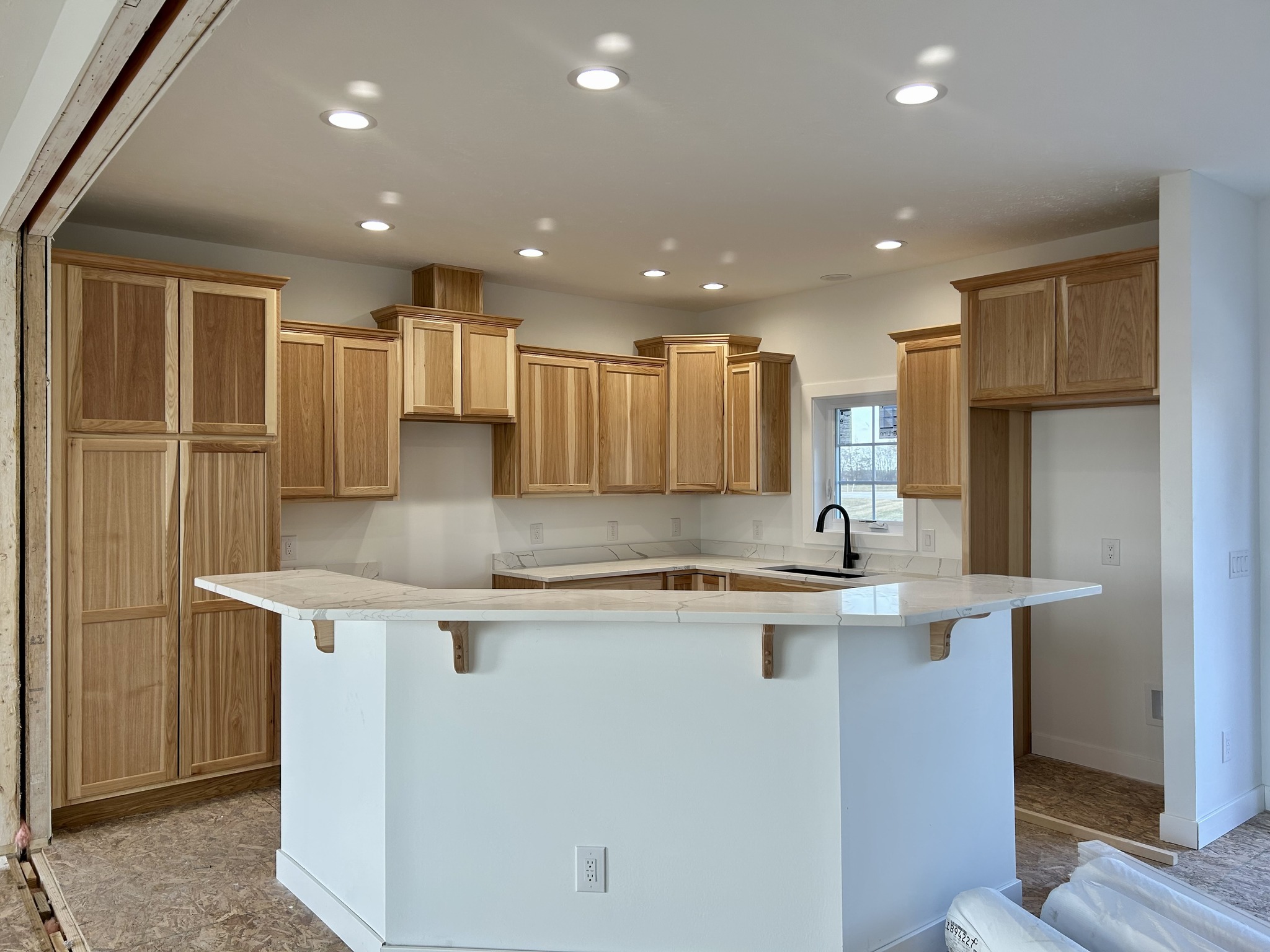 Modern kitchen interior with wooden cabinets and recessed lighting. A white countertop surrounds the space, providing a clean and inviting atmosphere.