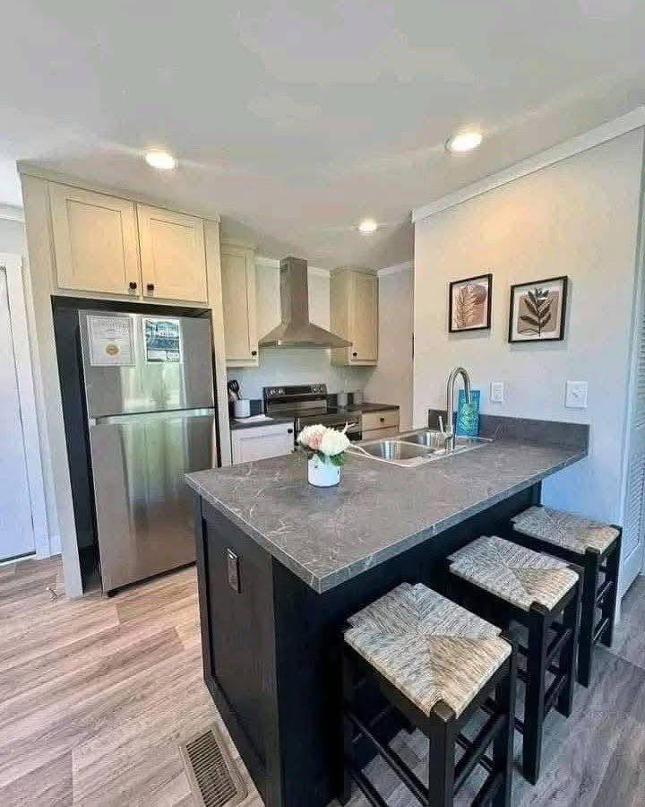 Modern kitchen with light cabinetry, stainless steel appliances, and a marble-patterned island with bar stools. Soft lighting and framed decor add elegance.