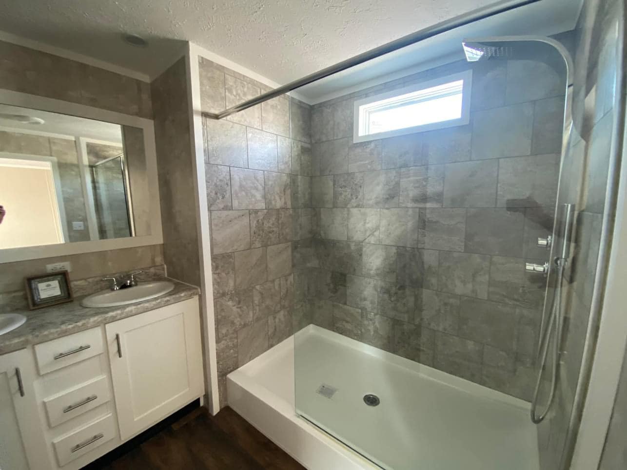 Modern bathroom featuring a spacious tiled shower with a glass door, a single sink vanity with a marble countertop, and a small window above.