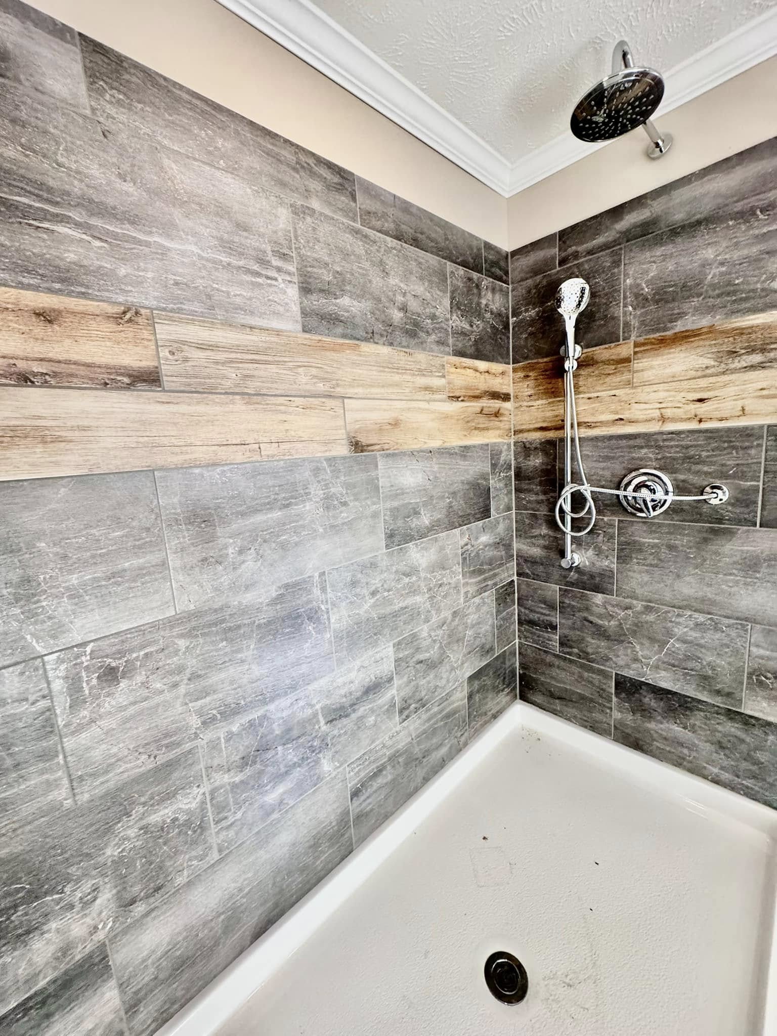 Shower area with rustic gray stone tiles and a horizontal wooden accent strip. Includes a chrome showerhead and controls, creating a modern, earthy feel.