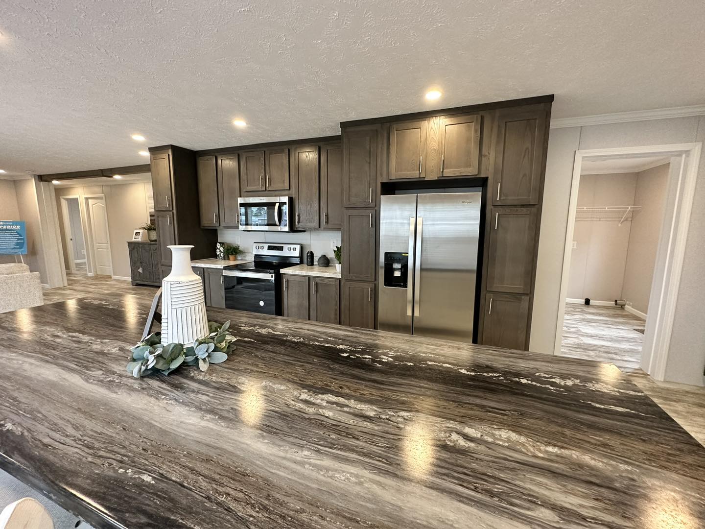 Modern kitchen with dark wood cabinets, stainless steel appliances, and a polished countertop. Decor includes a vase with greenery. Bright, spacious ambiance.