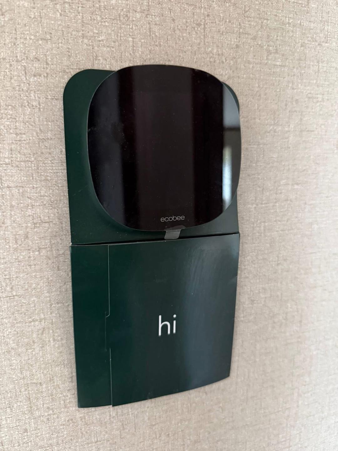 Smart thermostat on a textured wall, displaying "hi" with a sleek, modern design, reflecting minimalistic style and technological innovation.