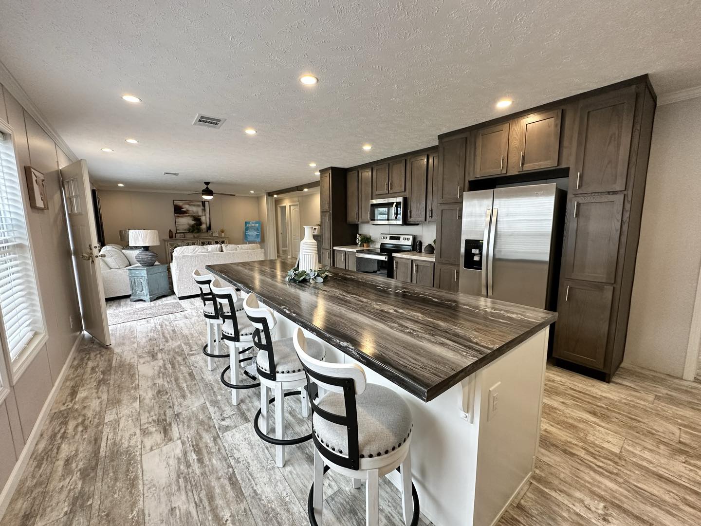 Modern bathroom with white bathtub, toilet, and brown cabinets. Features a marble countertop, large mirror, and wood-patterned floor, creating a clean, cozy feel.