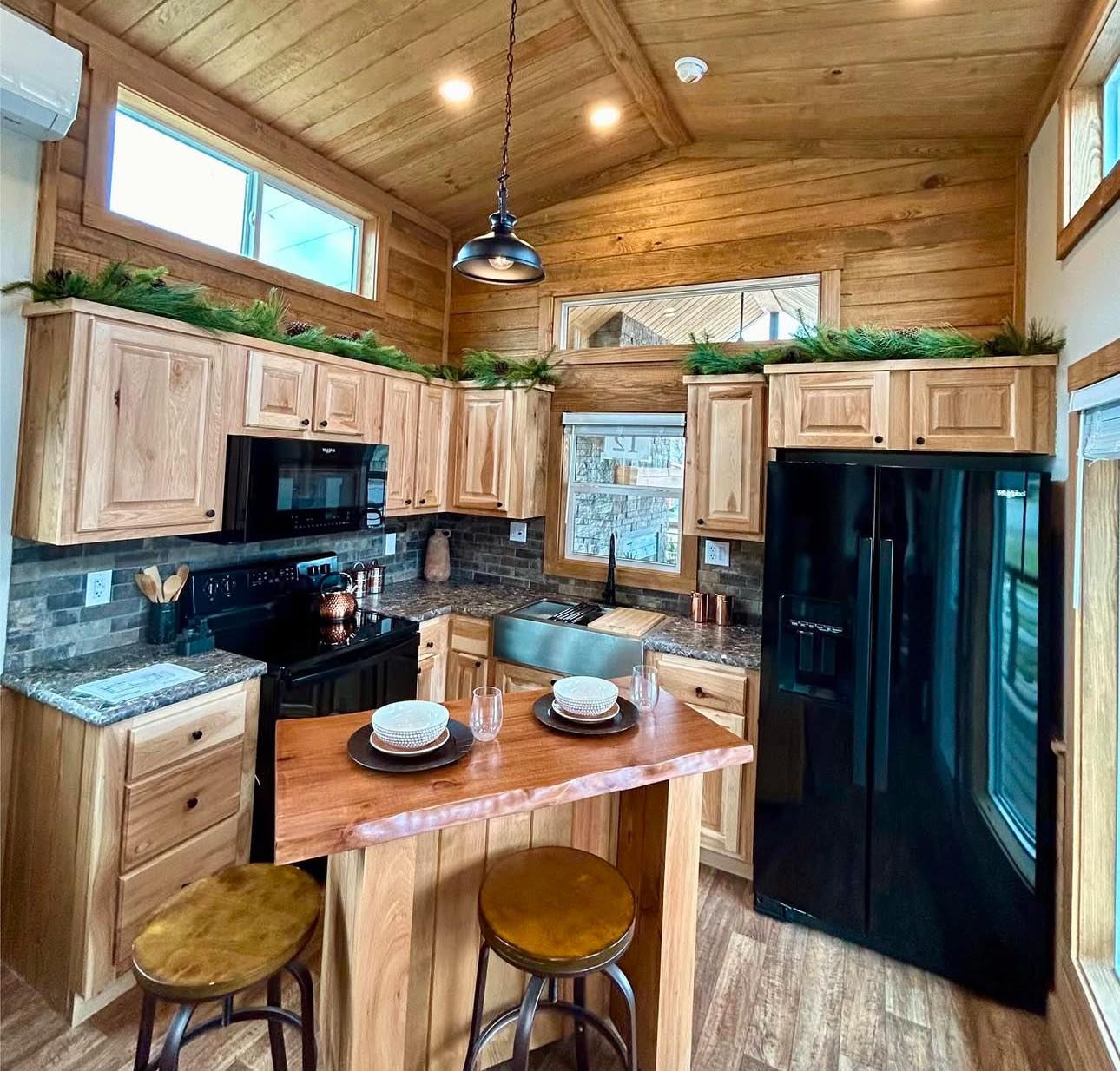 Cozy wooden kitchen with rustic charm, featuring pine cabinets, black appliances, stone backsplash, and a wooden island with stools. Warm, inviting atmosphere.